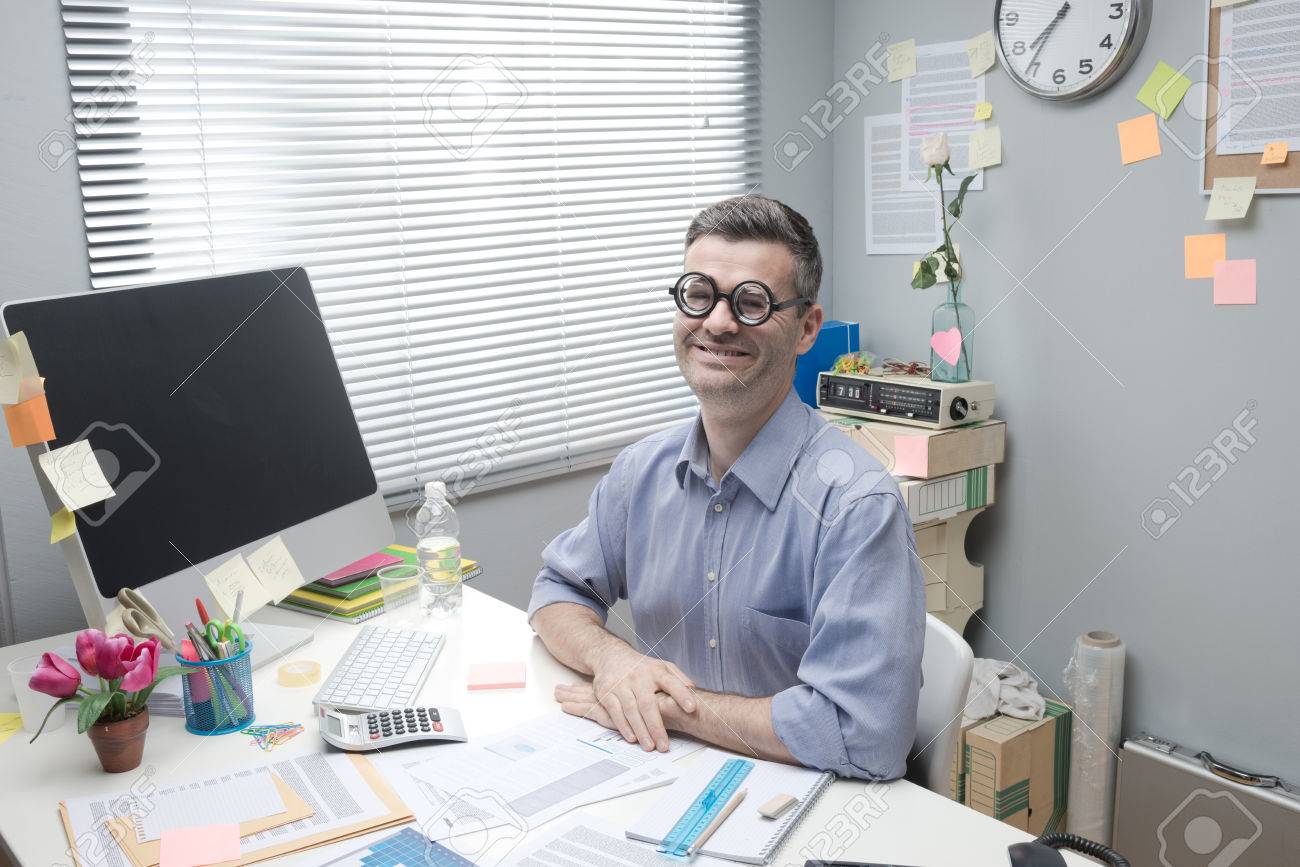 33304112-funny-nerd-businessman-at-desk-with-thick-glasses-smiling-at-camera-.jpg